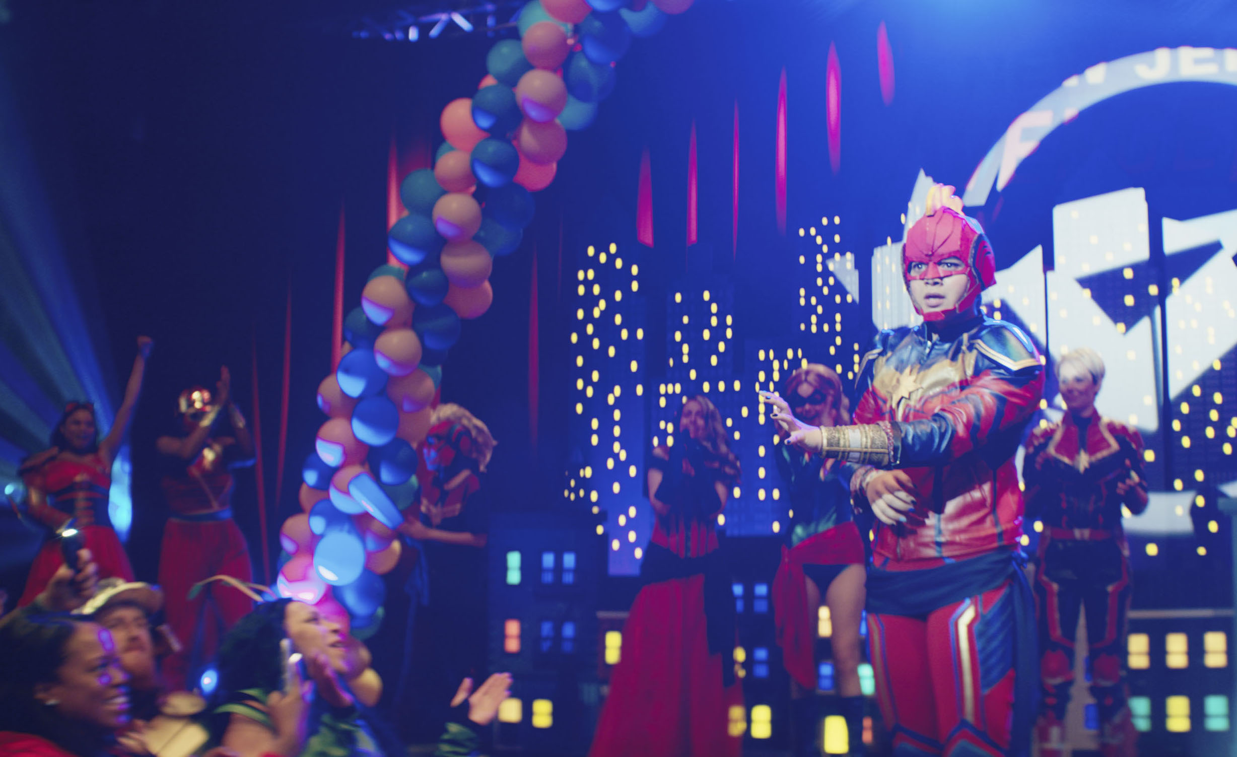 A teenage girl in a homemade Captain Marvel costume takes the stage at a convention cosplay contest;  still from 