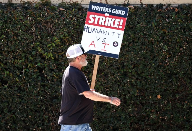 BURBANK, CALIFORNIA - AUGUST 16: A WGA (Writers Guild of America) sign reads 'Humanity vs. AI' as striking members picket outside Warner Bros. Studio on August 16, 2023 in Burbank, California. The Writers Guild of America reportedly met with the Alliance of Motion Picture and Television Producers yesterday with a response to the latest offer from the Hollywood studios over a collective bargaining agreement. (Photo by Mario Tama/Getty Images)